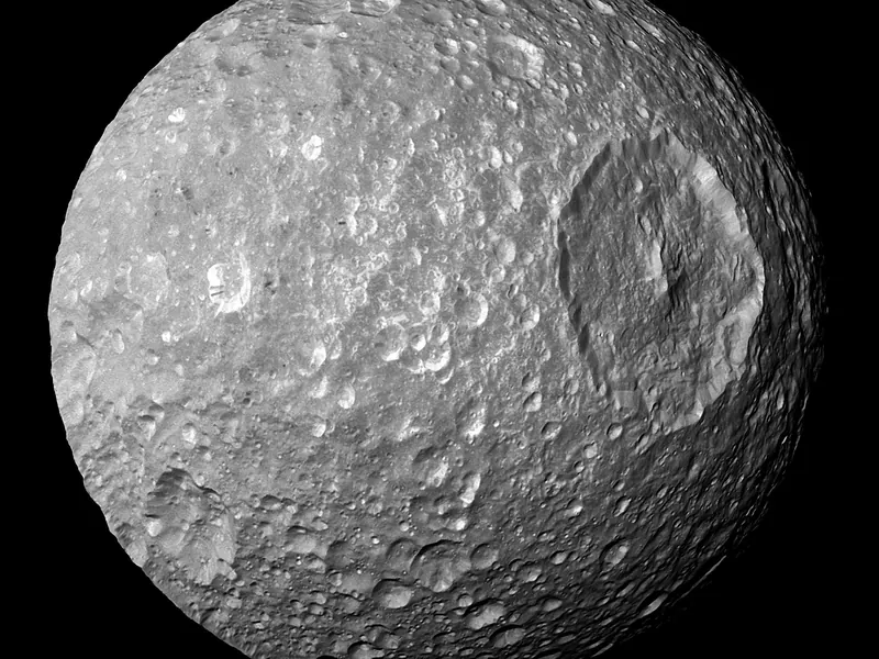 A grey cratered moon with one enormous crater on its face
