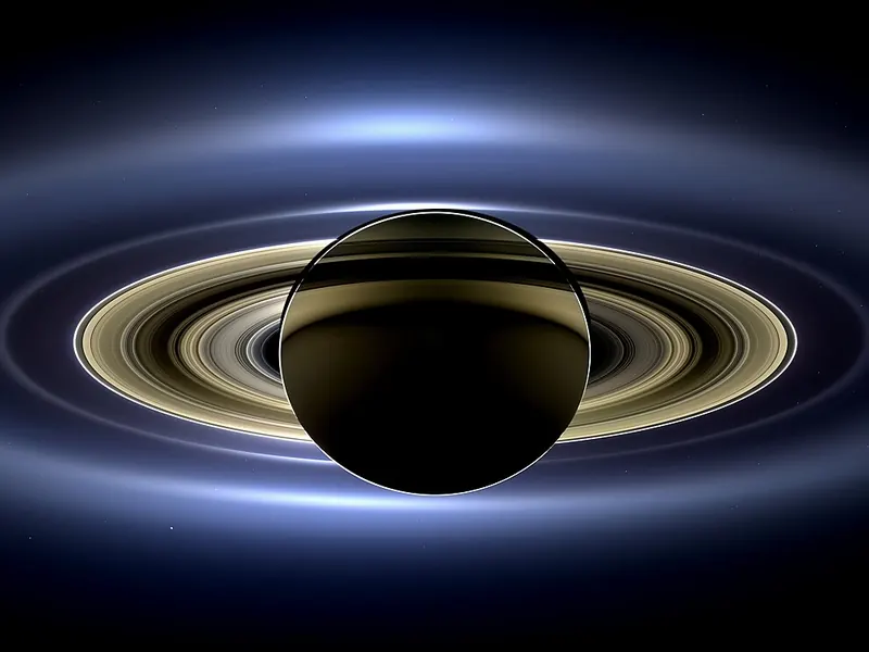 Saturn backlit by the Sun, its rings glowing, with Earth a tiny dot far away