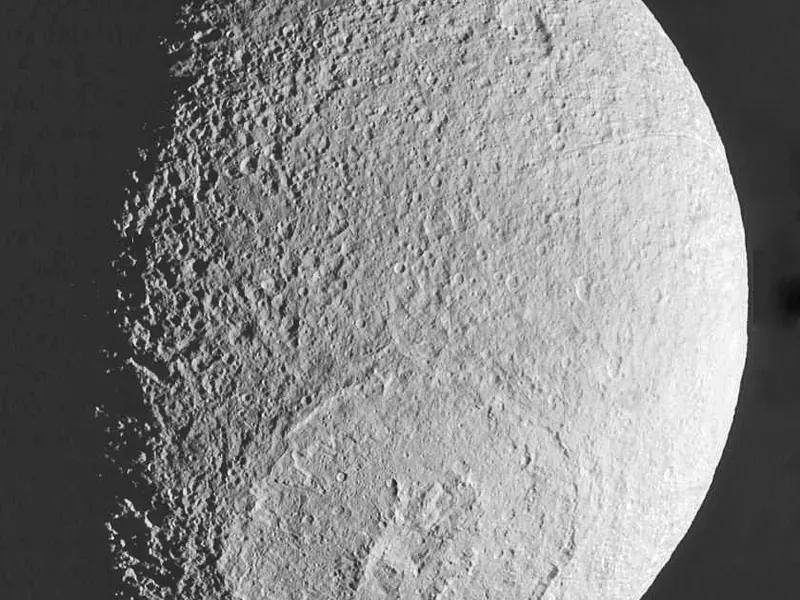 A pale grey icy moon with a huge crater