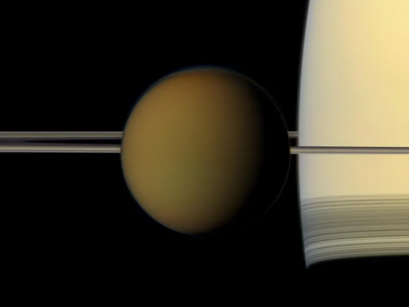 Titan’s small orange globe in front of Saturn, with the rings seen edge-on